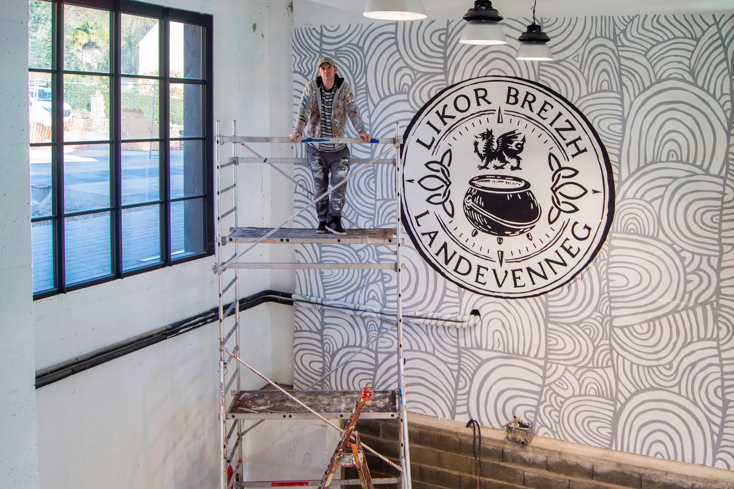 Décor mural d'art pariétal modernisé pour la distillerie Likor Breizh à Landévennec : arcs et lignes ondulantes noirs sur fond blanc autour d'un médaillon, peints sur échafaudage