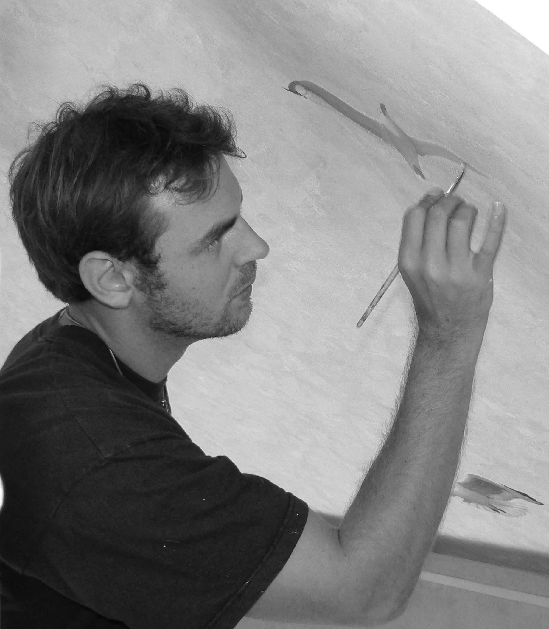 Portrait en noir et blanc d'un artiste peintre muraliste dessinant au pinceau sur un mur, formation au décor peint et à la fresque murale