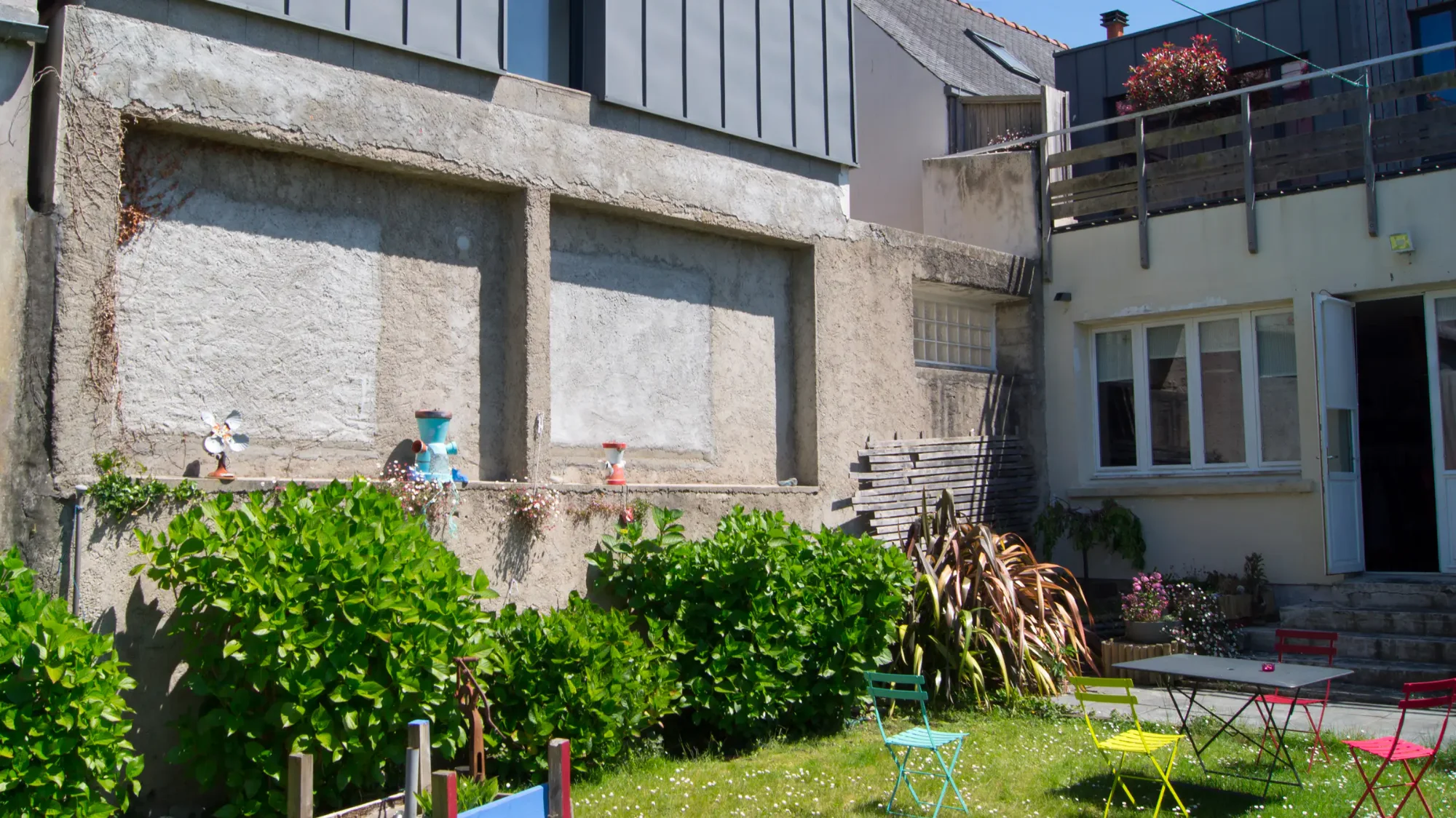 Avant, jardin d'une crêperie à Plestin-les-Grèves, mur de béton brut, hortensias et chaises colorées